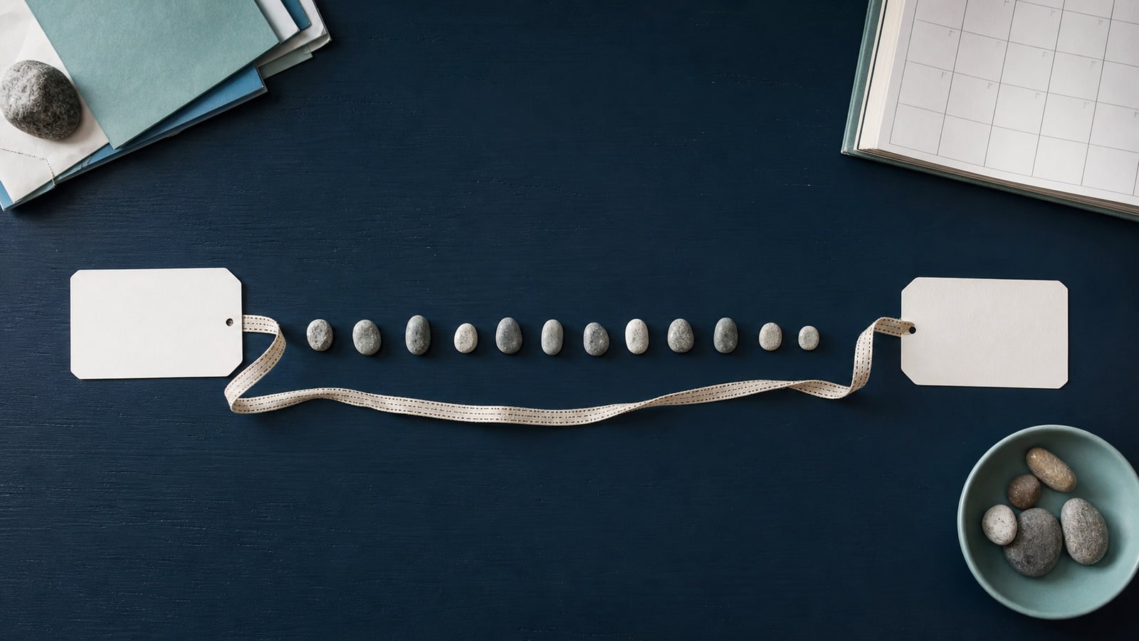 Two blank date cards are connected by stones and measuring tape across a navy worktable.